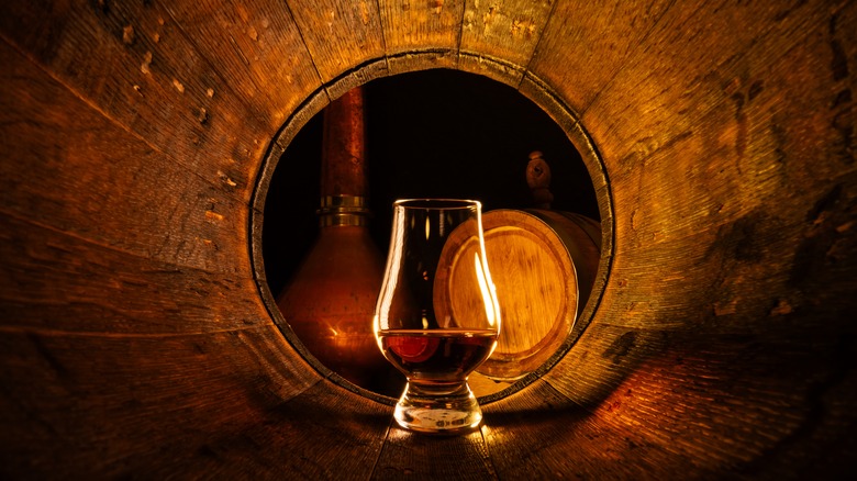 Glass of Scotch whisky in an oak barrel