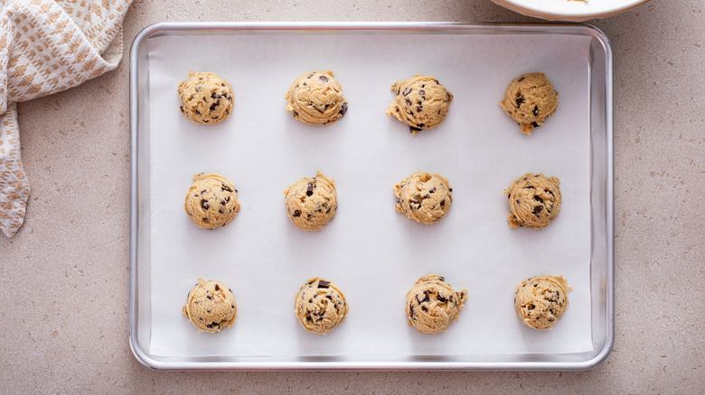 A sheet pan with a layer of parchment paper holds several balls of cookie dough