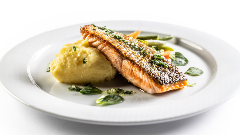 Baked salmon filet on a plate with vegetables and sauce.