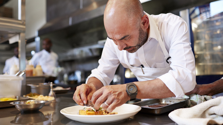 A chef plating food in a kitchen.