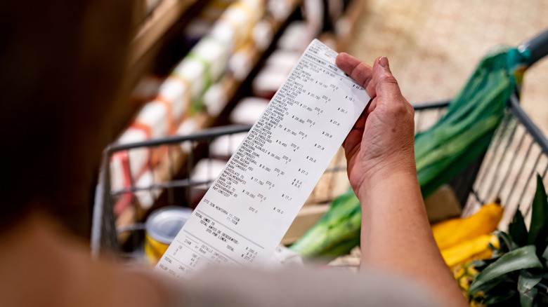 A hand holds a grocery receipt above a shopping cart