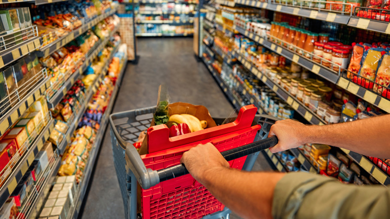 Arms push a shopping cart through a grocery store aisle