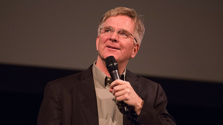 Rick Steves holding a microphone presenting on-stage