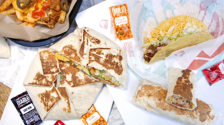 A variety of Taco Bell food items sit on their wrappers with hot sauce