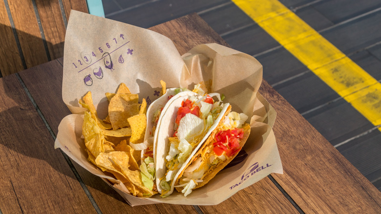 A basket of Taco Bell tacos and chips sits on a wooden table outside