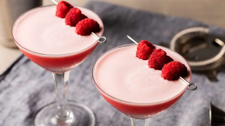 Two pink cocktails topped with egg white foam and fresh raspberries as garnish