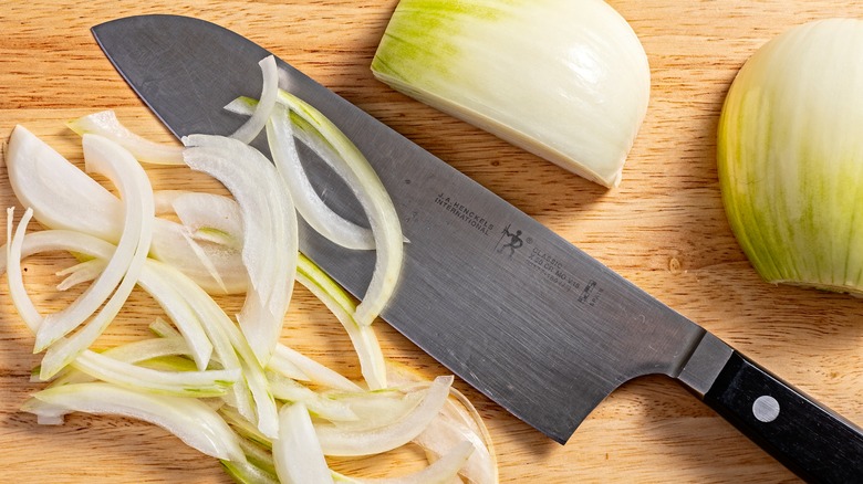 Some thinly sliced onion on a board with a kitchen knife