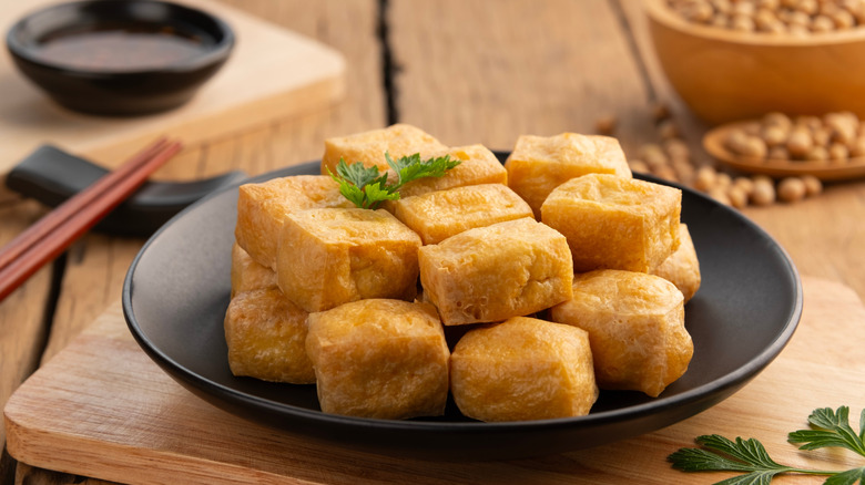 A plate of crispy fried tofu with a sprig of fresh parsley