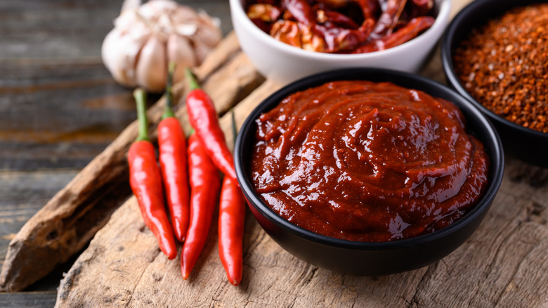 A bowl of gochujang next to red chile peppers