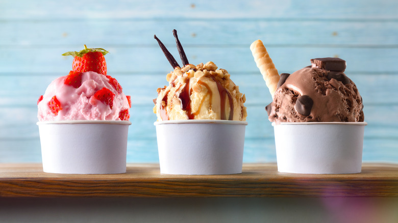 Three glasses of ice cream with strawberry, vanilla and chocolate balls decorated on a wooden table and blue slatted background. Front view.