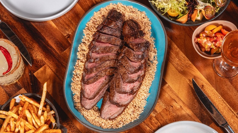 Two grilled picanha steaks on restaurant table, sides, cocktails