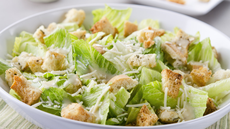 A bowl of Caesar salad has chopepd romaine lettuce, croutons, and shredded Parmesan cheese