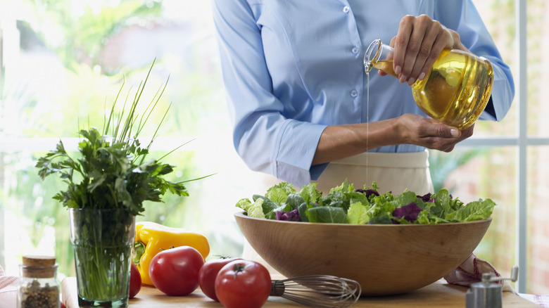 A chef pours a light vinaigrette over a bowl of leafy greens in a kitchen