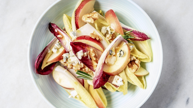 A salad with radicchio and endive greens, apple slices, walnuts, and blue cheese crumbles