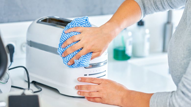 Woman wiping off outside of white toaster