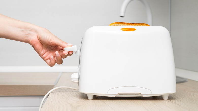Hand pressing down lever of white toaster