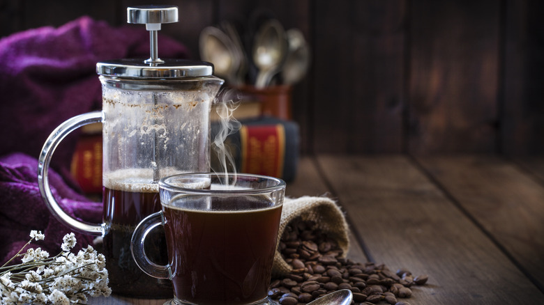 French press beside steaming cup of coffee