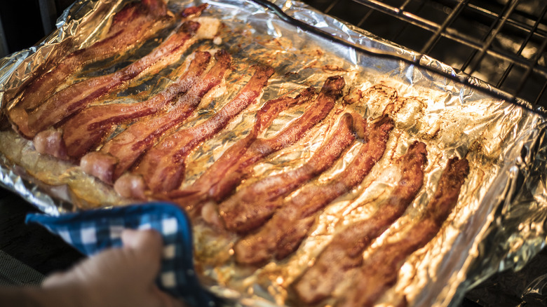 Strips of bacon cooking in an oven on a foil lined tray