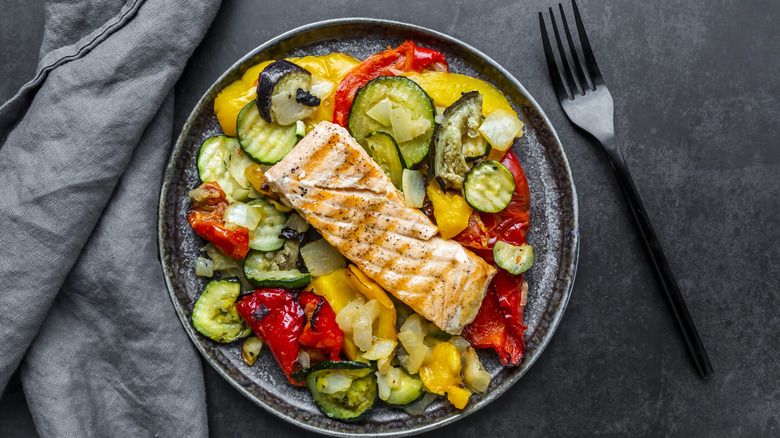 A plate of salmon and roasted vegetables on a slate-gray table