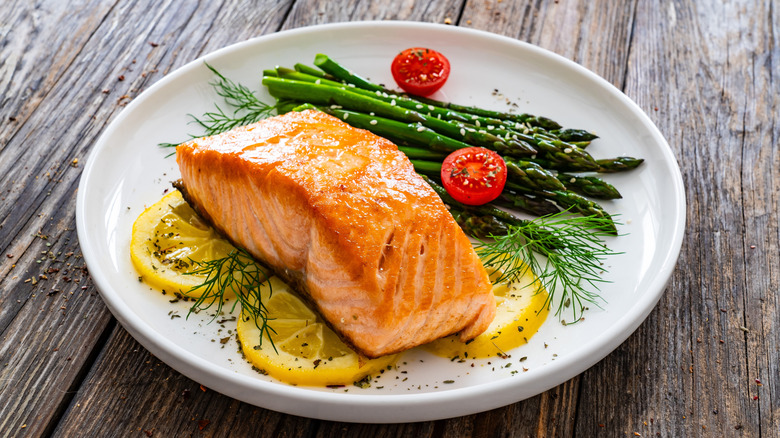 A plate of cooked salmon with asparagus, dill, cherry tomatoes, and lemon slices