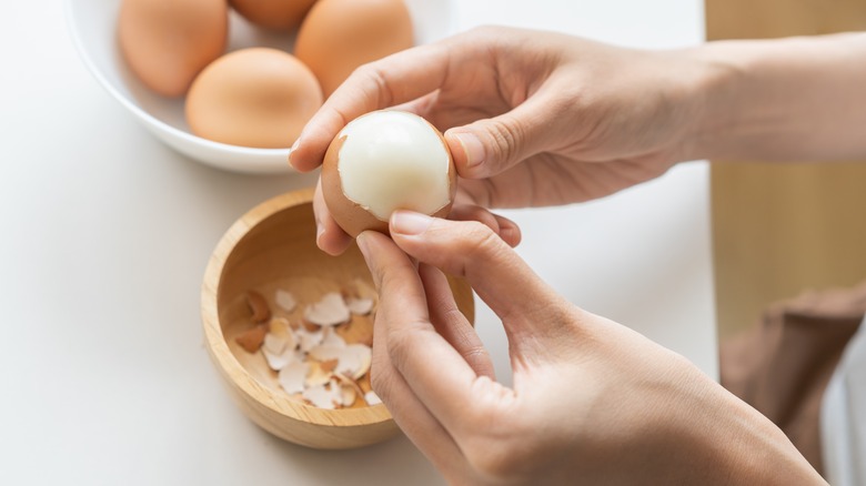 Close-up of woman's hands peeling brown hard-boiled eggs