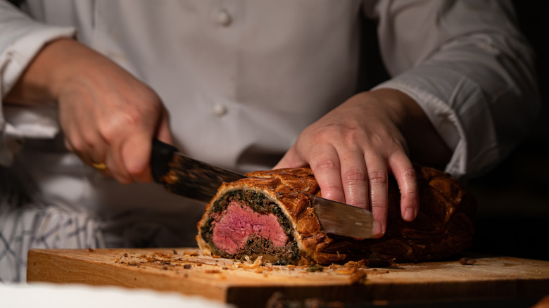 Chef cutting into beef Wellington with a knife