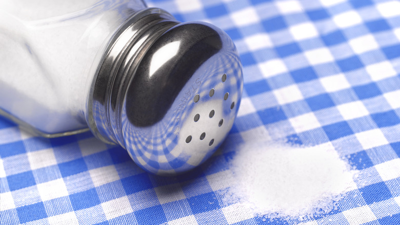 Salt spilled from a tipped over salt shaker on a blue checkered tablecloth