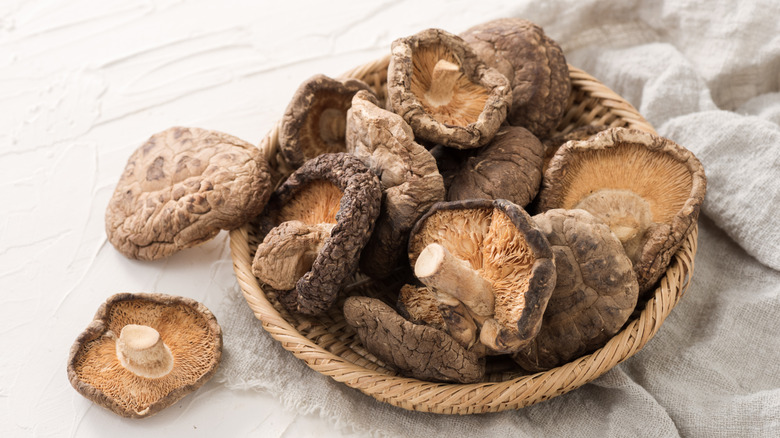 Dried shiitake mushrooms sit in a pile in a shallow woven basket