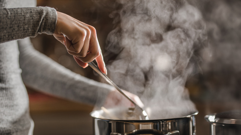 A woman stands before a simmering pot on a stove, stirring