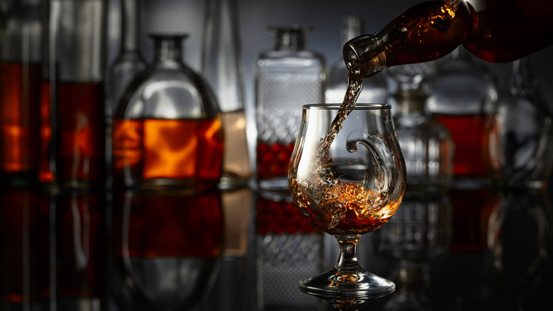 Cognac being poured into a glass with bottles in the background