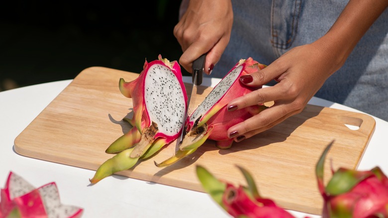 Person slicing whole dragon fruit on wooden cutting board