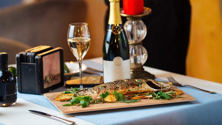 Grilled sea bass on white table cloth with champagne
