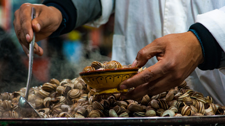 Large pan full of escargot being served into smaller bowl
