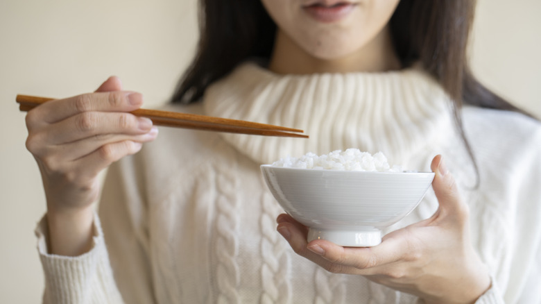 woman holding bowl of rice and chopsticks