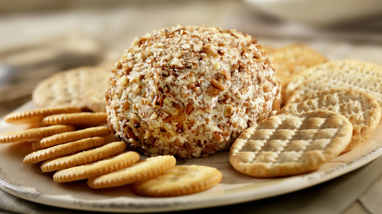 Cheese ball surrounded by an assortment of crackers on a white plate.