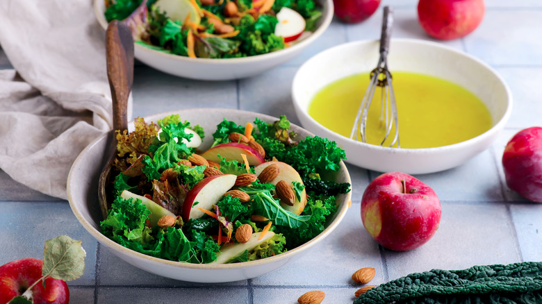 Crunchy kale, apple, and walnut salad in a bowl with a separate bowl containing the salad dressing