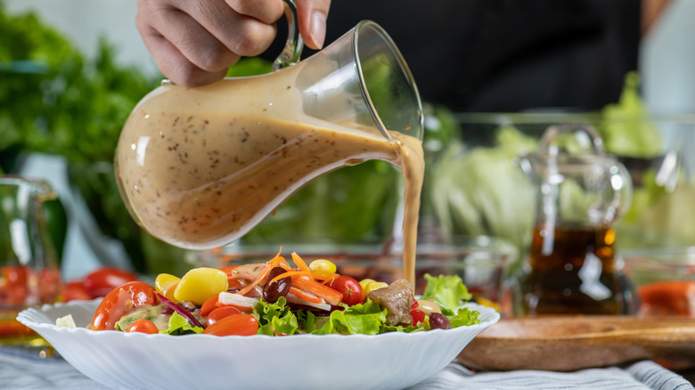 A hand pouring salad dressing over fresh greens and vegetables