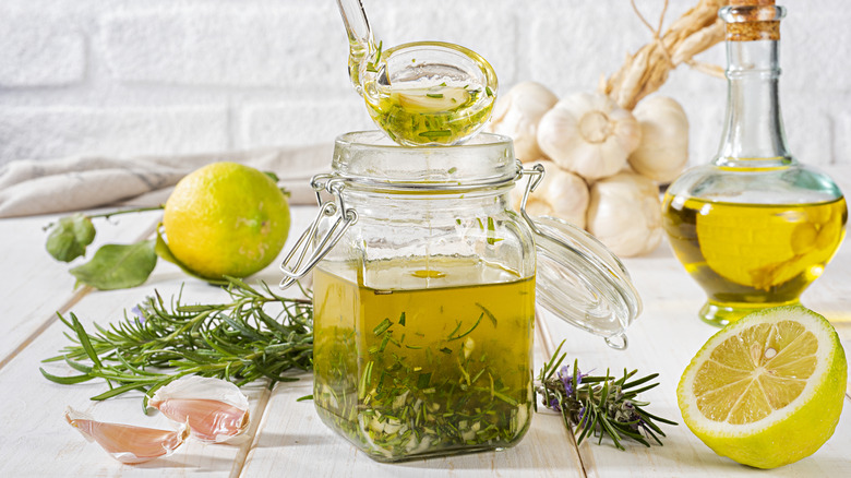 A homemade vinaigrette with herbs in a glass jar surrounded by ingredients