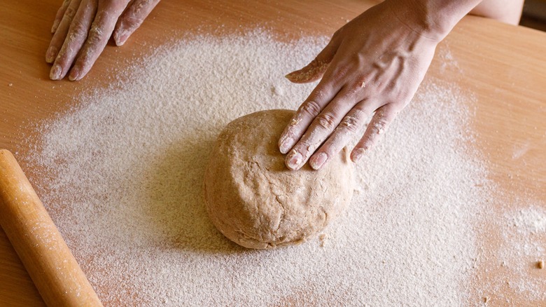 hands touching dough on a floured surface