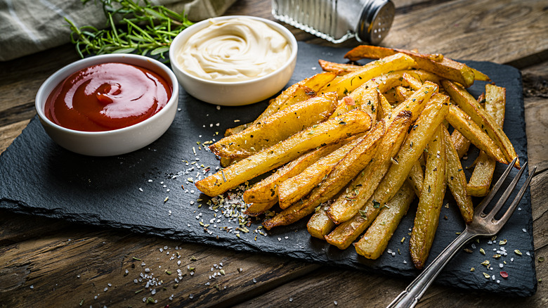 Homemade french fries are covered with fresh seasoning and sit beside some ketchup and mayonnaise