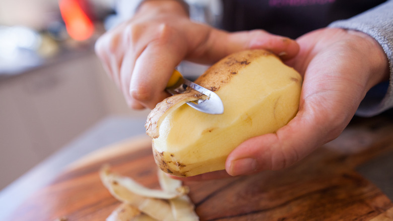 A person peels a russet potato