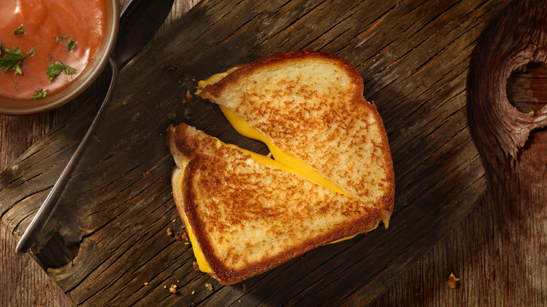 A grilled cheese sandwich cut in half diagonally on a wooden board.