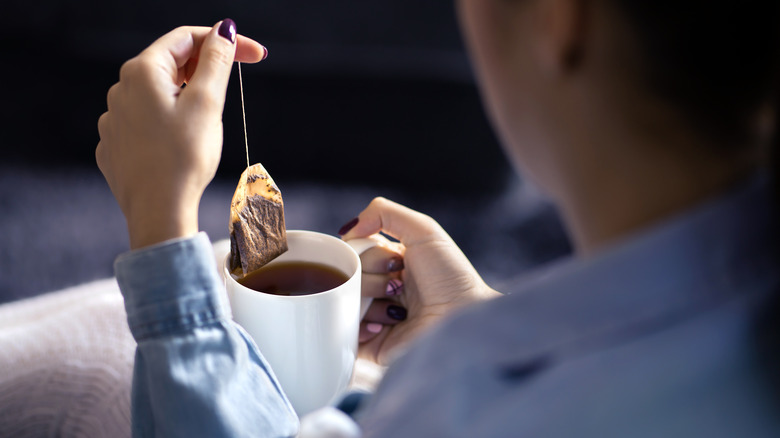 Woman holds white cup and steeps tea bag in dark tea