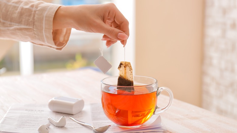 Female hand dips tea bag in clear glass with hot tea