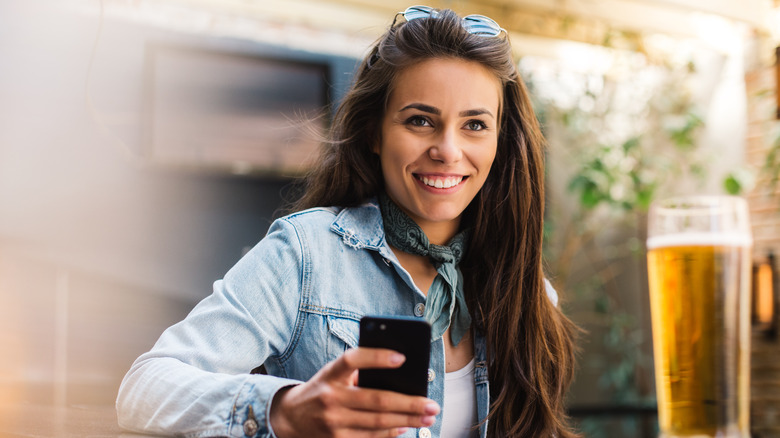 a smiling woman wearing a jean jacket drinking a beer