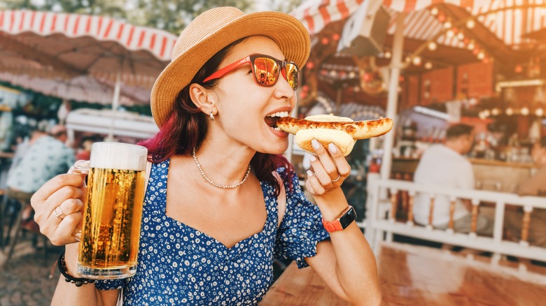 a woman eating a bratwurst and drinking a beer