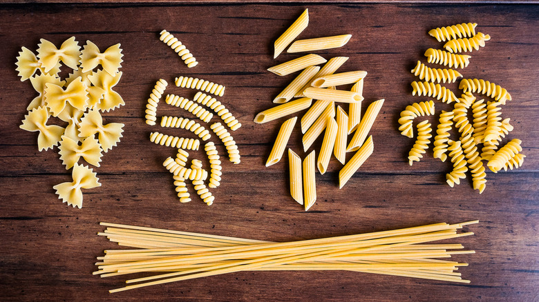 Variety of types and shapes of dry Italian pasta - fusilli, spaghetti, farfalle and penne, top view. Uncooked whole wheat Italian pasta.