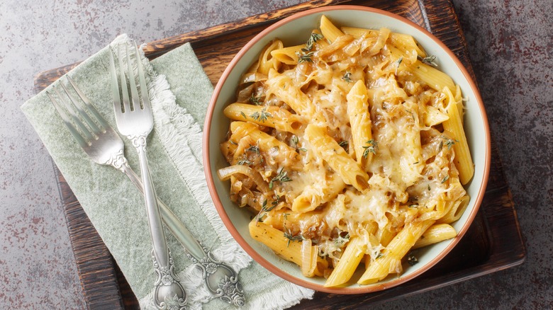 Delicious French onion pasta penne with caramelized onions, fragrant thyme, garlic and gruyere cheese close-up on a bowl on a wooden board. Horizontal top view from above