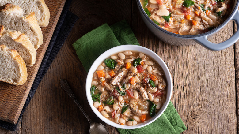 A bowl of bean soup with veggies on a green napkin.