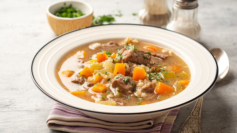 Beef and barley soup with vegetables in a white bowl.